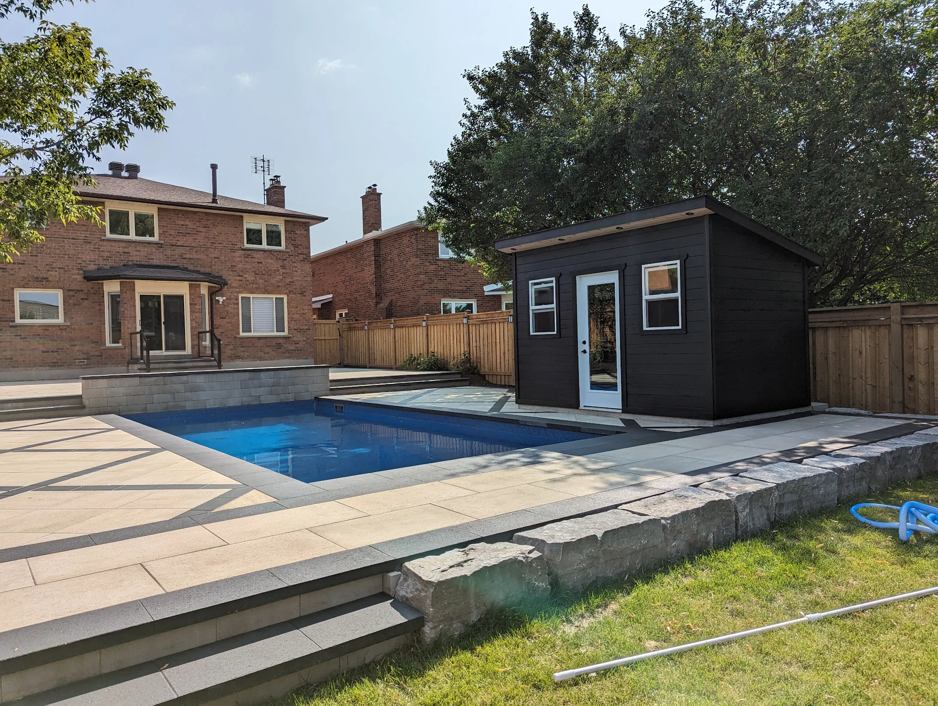 Inground pool with natural stone retaining wall and cabana in Toronto backyard